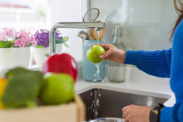 junge Frau wäscht Gemüse und Obst mit Wasser aus der Spüle - Foto, Bild