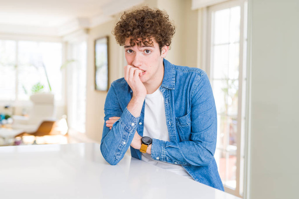 Young handsome man wearing casual denim jacket at home looking stressed and nervous with hands on mouth biting nails. Anxiety problem. - Fotografie, Obrázek