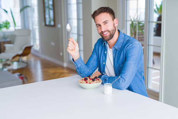 Handsome man having breakfast eating cereals at home and smiling - Foto, afbeelding