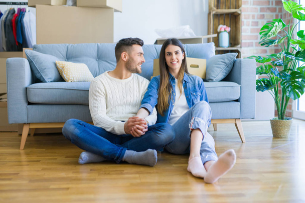 Jeune beau couple assis sur le sol du nouvel appartement, souriant d'amour heureux de déménager dans une nouvelle maison
 - Photo, image
