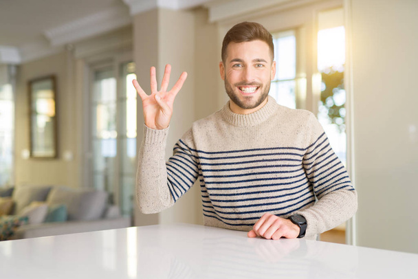 Молодой красивый мужчина дома показывается и показывает пальцами номер четыре, улыбаясь уверенно и счастливо
. - Фото, изображение