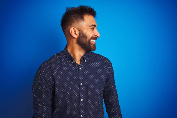 Jeune homme élégant indien portant chemise debout sur fond bleu isolé regardant de côté avec le sourire sur le visage, expression naturelle. Rire confiant
. - Photo, image