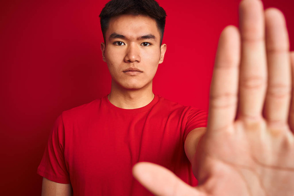 Fiatal ázsiai kínai ember visel póló állva az elszigetelt vörös háttér nyílt kézzel csinál jelet a súlyos és magabiztos kifejezés, védelmi gesztus - Fotó, kép