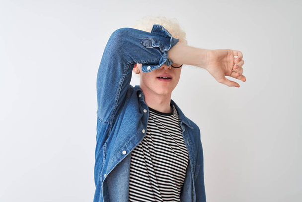 Mladý albín plavovlasý muž, který nosí džínou košili a brýle na izolované bílé pozadí zakrývající oči paží, vypadá vážně a smutně. Koncepce nespatné, skrývání a odmítání - Fotografie, Obrázek