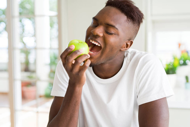 Young african american man eating a healthy green apple - Fotó, kép