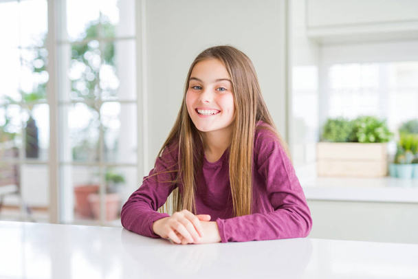 Mooi jong meisje Kid op witte tafel met een gelukkige en koele glimlach op het gezicht. Gelukkige persoon. - Foto, afbeelding