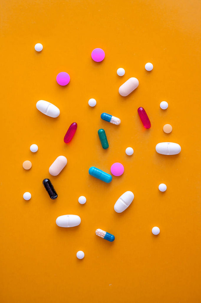 verspreid een verscheidenheid van multi-gekleurde pillen in een geel-oranje achtergrond. Uitzicht van bovenaf. Close-up - Foto, afbeelding
