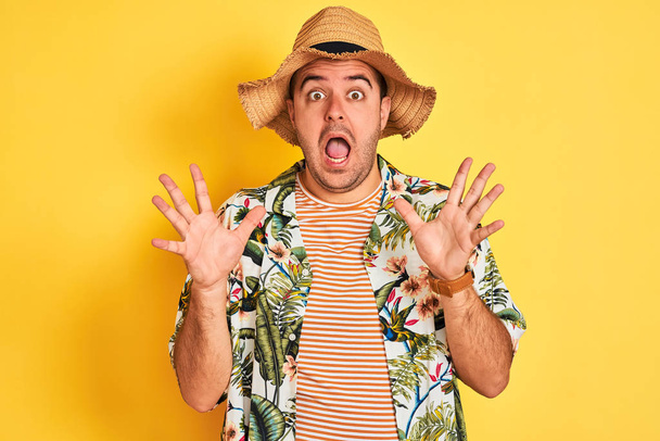Jeune homme en vacances portant chemise d'été et chapeau sur fond jaune isolé célébrant fou et étonné pour le succès avec les bras levés et les yeux ouverts hurlant excités. Concept gagnant
 - Photo, image