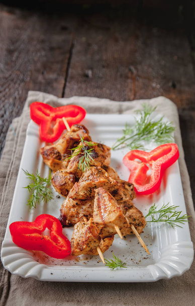 Ζουμερό κρέας-κοτόπουλο σουβλάκια σε ξύλινα καλαμάκια σε λευκό πιάτο σε σκούρο ξύλινο φόντο - Φωτογραφία, εικόνα