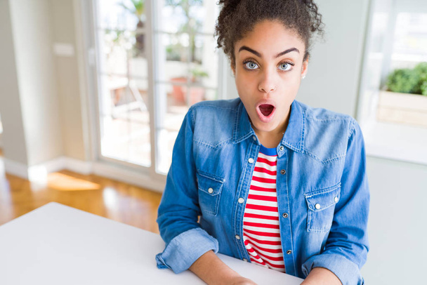 Beautiful young african american woman with afro hair wearing casual denim jacket afraid and shocked with surprise expression, fear and excited face. - Photo, Image