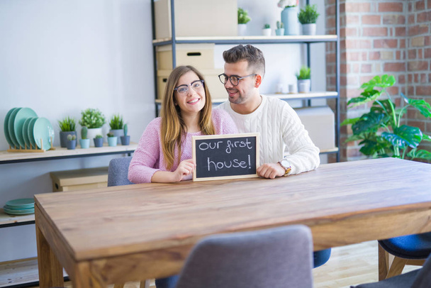 junges Paar hält Tafel mit unserem ersten Haustext, sehr glücklich über Umzug in neue Wohnung - Foto, Bild
