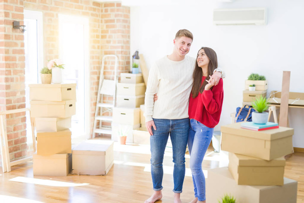Beautiful young couple moving to a new home, standing on new aparment around cardboard boxes, hugging smiling happy and in love - Φωτογραφία, εικόνα