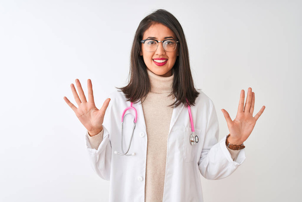 Mujer doctora china vistiendo abrigo y estetoscopio rosa sobre fondo blanco aislado mostrando y señalando hacia arriba con los dedos número diez mientras sonríe confiado y feliz
. - Foto, Imagen