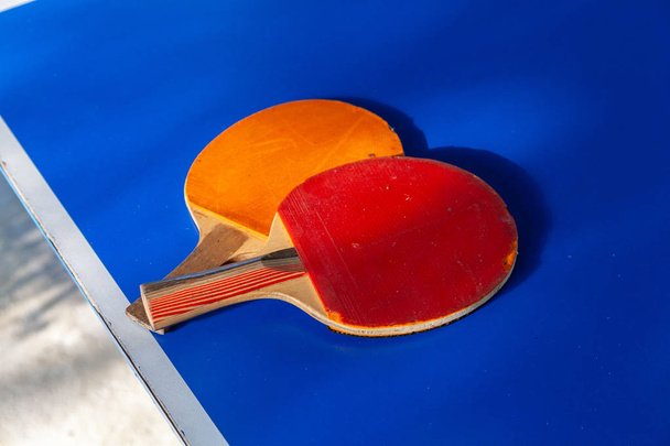Gros plan de deux raquettes de ping-pong rouge et orange couchées sur une table bleue
 - Photo, image