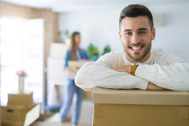 Young couple moving to a new home, handsome man smiling leaning on cardboard boxes - Фото, зображення