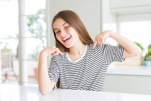 Hermosa niña joven con rayas camiseta mirando confiado con sonrisa en la cara, señalándose con los dedos orgullosos y felices
. - Foto, Imagen