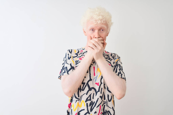 Mladý albín plavovlasý muž s barevnou košilí, stojící nad izolovaným bílým pozadím, šokoval ústa s rukama na omylu. Tajný koncept. - Fotografie, Obrázek