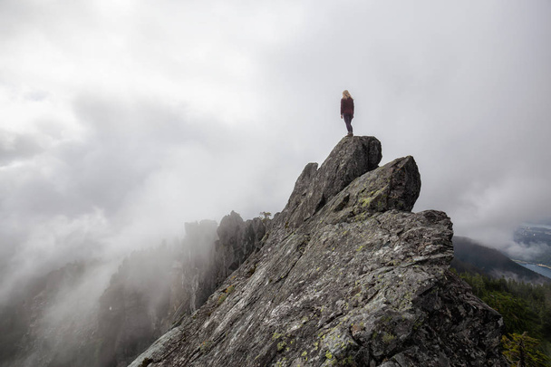 Adventurous Girl on top of a rugged rocky mountain during a cloudy summer morning. Taken on Crown Mountain, North Vancouver, BC, Canada. - Foto, imagen