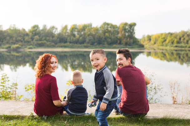 Concept de parentalité, nature, personnes - famille avec deux fils assis près du lac
 - Photo, image