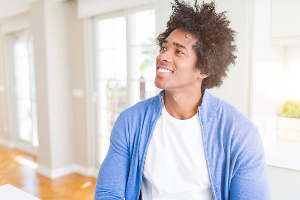 Αφρικανική αμερικανική άνδρα στο σπίτι χαμογελώντας αναζητούν πλευρά και χτυπητός μακριά σκέψης. - Φωτογραφία, εικόνα