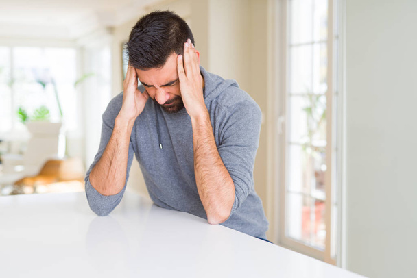 Pohledný, hispánský muž v neformálním tričku doma trpícím bolestí hlavy a vystresovaný, protože bolest a migréna. Ruce na hlavu. - Fotografie, Obrázek
