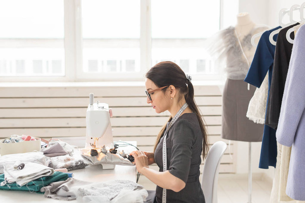 人とファッションのコンセプト - 若いドレス メーカー女ミシンで服を縫う - 写真・画像