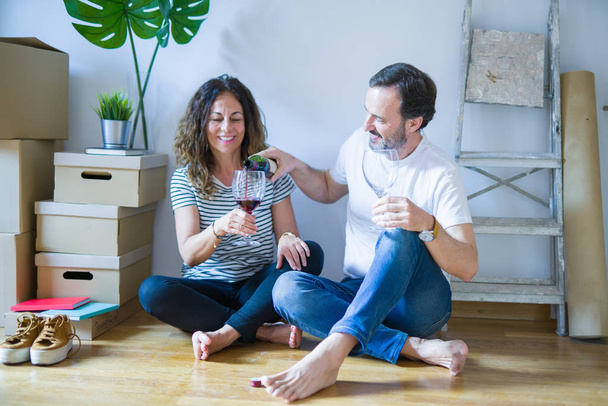 Középkorú Senior romantikus pár szerelmes ül az apartman padló dobozok körül, ünnepli iszik egy pohár bort mosolyogva boldog költöznek egy új otthon - Fotó, kép