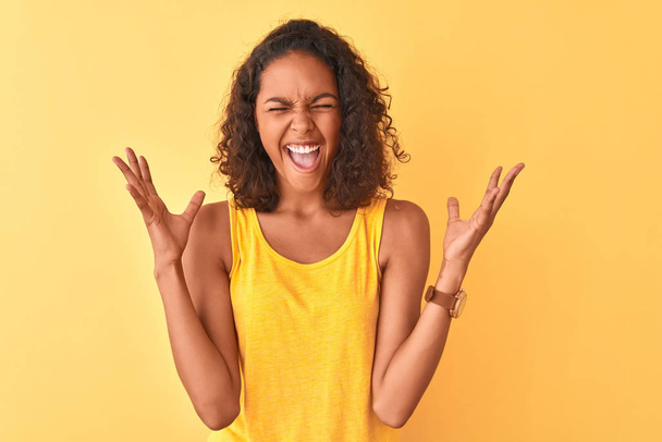 Mladá brazilská žena nosí tričko na izolovaném žlutém pozadí a oslavuje šílené a bláznivé úspěchy se zdviženýma rukama a zavřenýma očima vzrušených. Koncepce vítězů - Fotografie, Obrázek