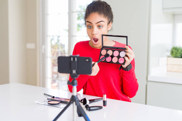 Joven afroamericana influencer mujer grabación maquillaje tutorial asustado en shock con una cara sorpresa, asustado y emocionado con la expresión de miedo
 - Foto, imagen