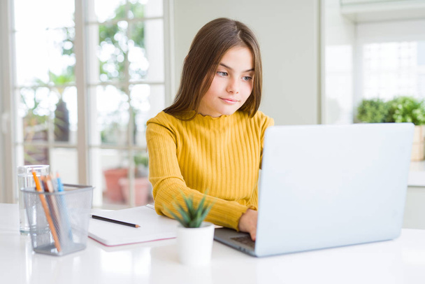 Piękna młoda dziewczyna studiuje do szkoły za pomocą komputera laptop z pewnym wyrazem na inteligentne myślenie twarzy poważne - Zdjęcie, obraz