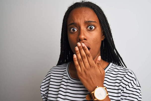 junge afrikanisch-amerikanische Frau in gestreiftem T-Shirt vor isoliertem weißem Hintergrund, Mund bedeckt mit Hand geschockt vor Scham über Fehler, Ausdruck von Angst, Angst in der Stille, geheimes Konzept - Foto, Bild