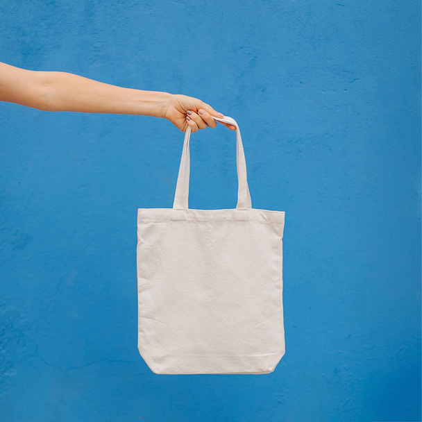 Woman holding canvas tote bag on bright blue background in the city. Reusable eco bag. Eco friendly concept. - Photo, image