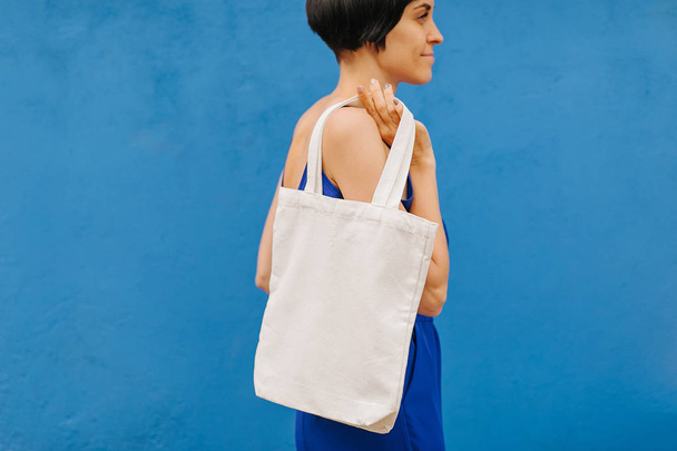 Woman holding canvas tote bag on bright blue background in the city. Reusable eco bag. Eco friendly concept. - Fotografie, Obrázek