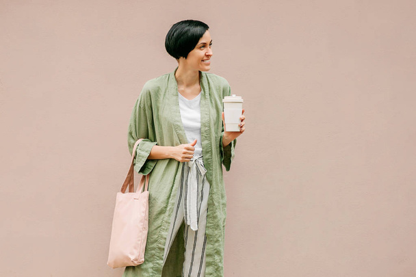 Woman with short hair holding reusable coffee cup and eco bag enjoying morning. Eco friendly concept. - Foto, immagini