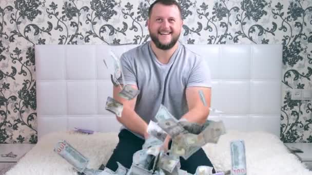 αρσενικό απολαμβάνει τεράστιο πλούτο. άνθρωπος ρίχνει πολλά χαρτονομίσματα σε ένα λευκό κρεβάτι, πετάει χρήματα - Πλάνα, βίντεο