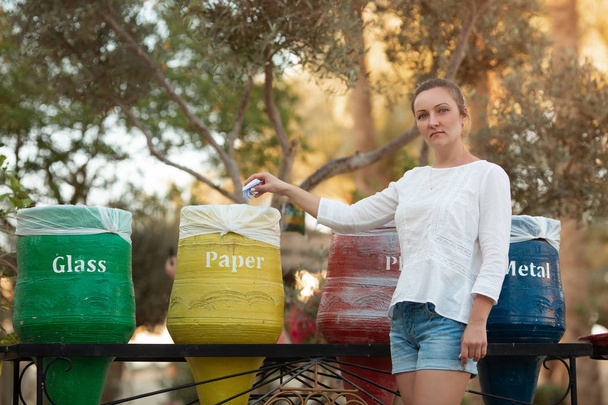 Młoda kobieta pozbywająca się śmieci, wrzucając ją do żółtego dekoracyjnego pojemnika, jest po prawej stronie. Ładna kobieta w casual noszenia i trampki opieki dla środowiska. Daje przykład, jak pomóc - Zdjęcie, obraz