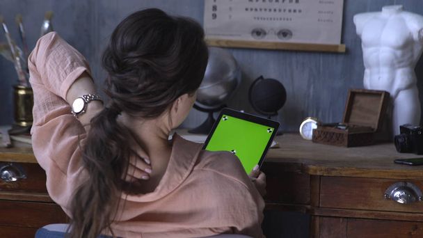 Vue de l'arrière de la jolie fille assise à la table et utilisant une tablette d'ordinateur avec écran vert chromatique. Images d'archives. Écran à clé chroma pour le placement de votre propre contenu
. - Photo, image