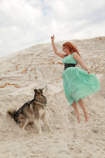 Concepto divertido de los mejores amigos. Feliz joven mujer camina en el desierto con el perro grande malamute al aire libre
 - Foto, Imagen