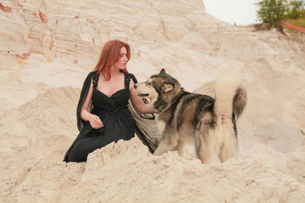 Concepção engraçada dos melhores amigos. Jovem feliz pessoa feminina caminha no deserto com cão grande malamute ao ar livre
 - Foto, Imagem