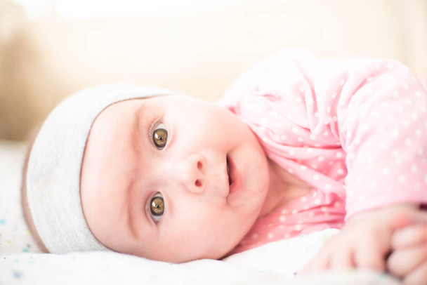 Adorable baby girl in pink lie on side and looking towards camera and smiling. Health concept - Foto, afbeelding