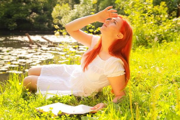 adolescente con i capelli rossi in cotone bianco vestire riposo e la lettura del libro in un parco estivo della città calda
 - Foto, immagini