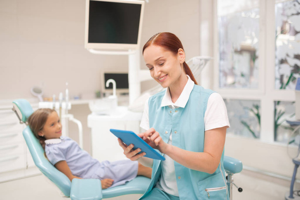 Dentist smiling while filling information on tablet - Фото, изображение