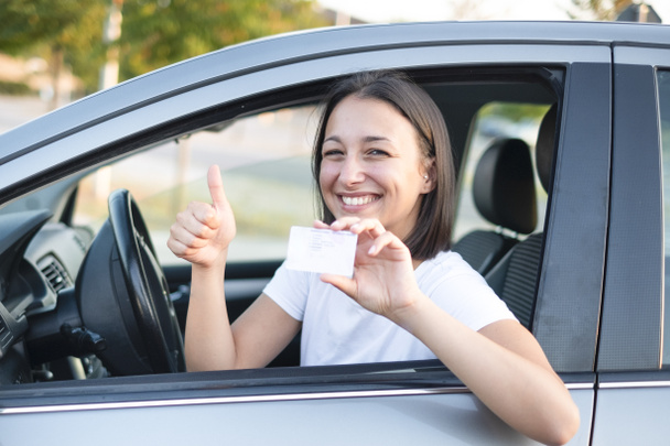 Young woman holding driver license in her car - Photo, Image