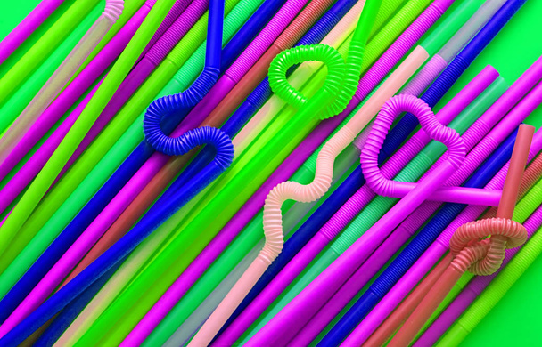 Tubos de cóctel de plástico de color con una parte flexible, por lo que pueden retorcerse en un nudo o en zigzag, o en forma de corazón, sobre un fondo verde. Colores modernos y neón de moda. Concepto ecológico
 - Foto, imagen