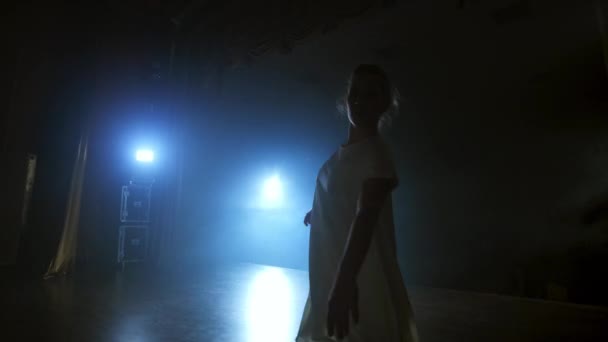 La cámara de zoom mueve a la bailarina a través del escenario con software y humo. Un ballet dramático moderno, una mujer con un vestido blanco gira sobre una pierna y salta
. - Imágenes, Vídeo