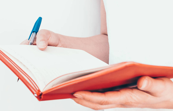 Woman's hands holding pen and red notepad on a white background.  - 写真・画像