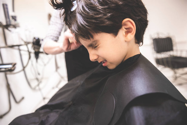 I don't like hair cut it hurts me little young child boy toddler at barbershop hairdresser saloon protesting against hair cut in pain and hurt scared painful experience first time hair cut close up - Foto, immagini