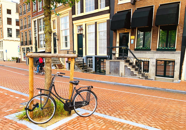 schwarzes fahrrad geparkt gegen einen baum in einer straße von amsterdam, niederland. Einsam verlassenes Fahrrad.  - Foto, Bild