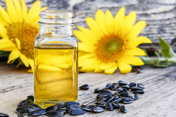 Sunflower oil in a glass jar with seeds and fresh flowers on a wooden background. Healthy foods and fats. - Photo, Image