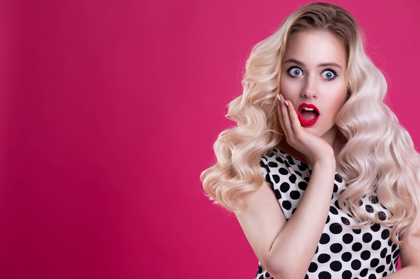 A woman with red bright lips suddenly touched her hand to her cheek. A beautiful girl with curly hair is surprised and shocked. Presentation of your product. Expressive facial expressions - Photo, image